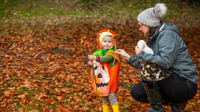A women and child bending down surrounded by autumn leaves.